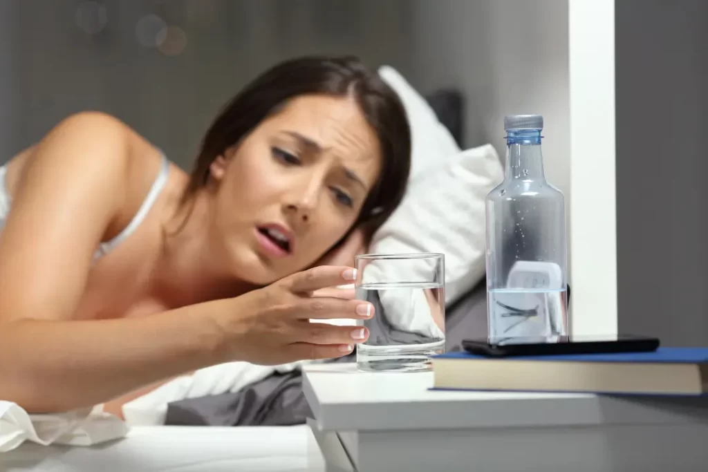 A dehydrated woman is trying to reach to the water glass.