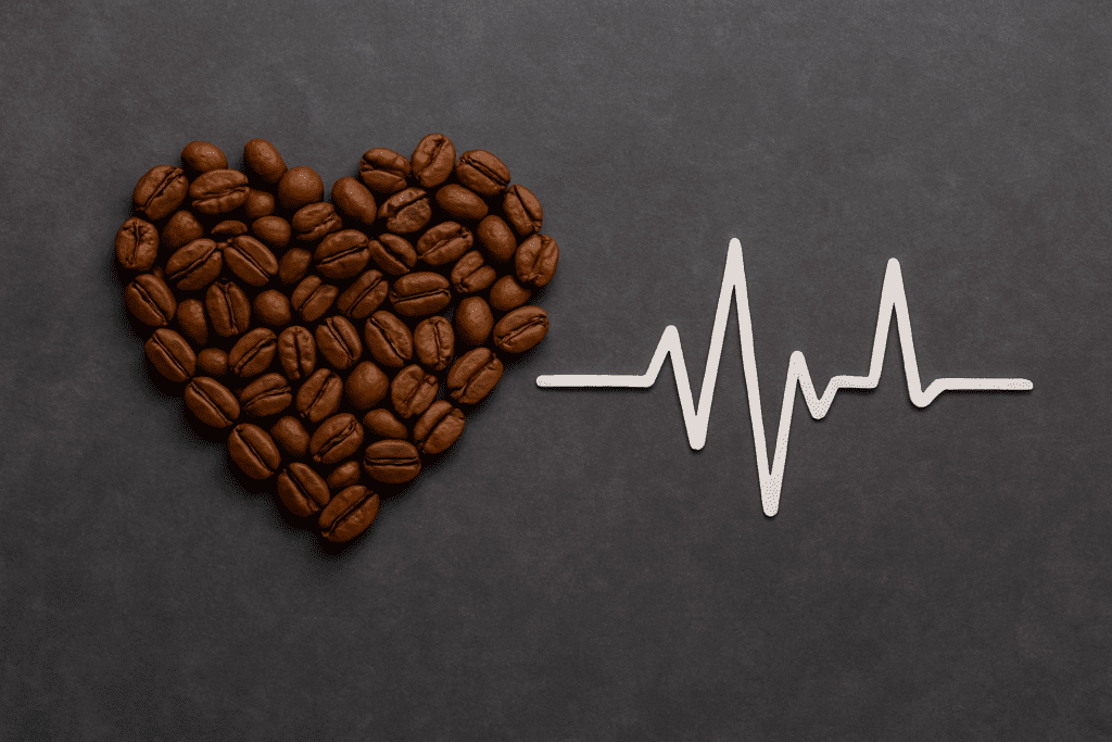A photograph captures a heart-shaped arrangement of coffee beans on the left and a white ECG line on the right, set against a dark gray background, symbolizing the debated relationship between caffeine and heart health.